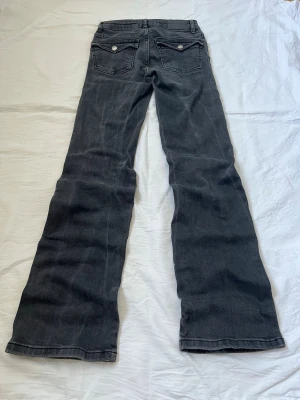 Svarta bootcut jeans med fickdetaljer - Svarta bootcut jeans med snygga fickdetaljer bak och klassisk femficksdesign. Jeansen har en lätt utsvängd passform och är tillverkade i denim med en tvättad look. Diskuterar gärna pris! ✨