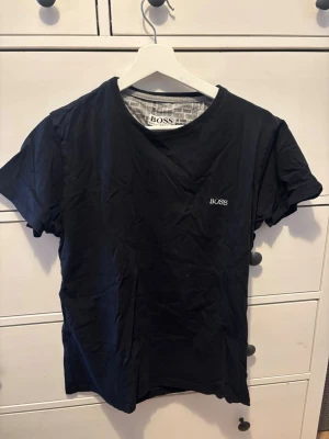 Svart t-shirt från BOSS - Klassisk svart t-shirt från BOSS med diskret logga broderad på bröstet. T-shirten har rund halsringning och korta ärmar. Tillverkad i mjuk bomull för en bekväm känsla och enkel att matcha med allt.
