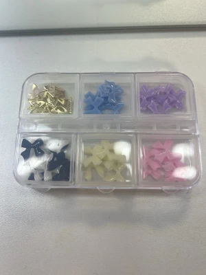 Nageldekorationer rosetter och fjäril  - Säljer ett set med små nageldekorationer i form av rosetter i olika färger: blå, vit, svart, gul, rosa och lila. Även en guldiga fjärilar. Kommer i en praktisk förvaringsbox. Perfekt för att skapa unika och kreativa nageldesigner. Materialet är plast och metall.