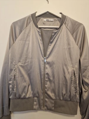 Silvrig bomberjacka från Gina Tricot - Snygg silvrig bomberjacka från Gina Tricot med glansigt tyg. För dig som vill ha en stilren och trendig look.