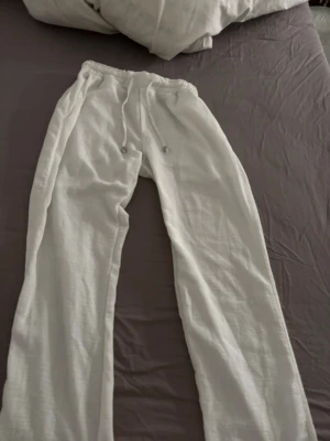 Vita linnebyxor med dragsko - Säljer ett par vita linnebyxor med avslappnad passform och elastisk midja med dragsko. Byxorna har raka ben och fickor både fram och bak. Perfekta för en chill och stilren look. Materialet är luftigt linne som känns svalt och skönt.
