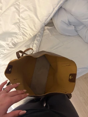 Brun shoppingväska i läderlook - Snygg shoppingväska i brun läderimitation med rymligt fack och magnetknäppning. Insidan är ljusgul och väskan har två handtag för enkel bärning. Perfekt för att få plats med allt du behöver under dagen.