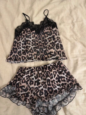 Leopardmönstrat loungewear-set - Snyggt loungewear-set med leopardmönster, består av ett linne med tunna axelband och spetsdetaljer samt matchande shorts med volangkant. Perfekt för en avslappnad dag hemma. Materialet känns lätt och luftigt.