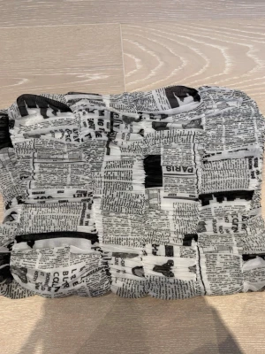 Svartvit bandeau topp  - Trendig bandeau topp i svartvitt med tidningsinspirerat tryck. Toppen är elastisk och har en scrunchad effekt som ger en cool och edgy look. Perfekt för dig som vill sticka ut med ett unikt plagg. Materialet känns lätt och stretchigt.