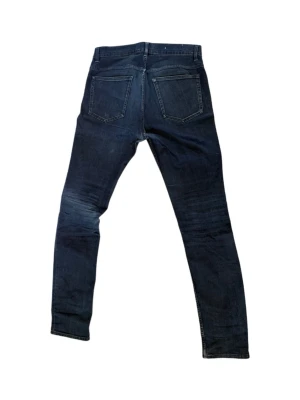 Mörkblå skinny jeans Acne Studios 29/34 - Säljer ett par mörkblå skinny jeans från Acne Studios med klassisk femficksdesign och dragkedja. Jeansen har raka ben och är tillverkade i denim med stretch för extra komfort. Perfekt för dig som gillar en stilren och modern look. Hål som visas på bilden med kommer tyvärr