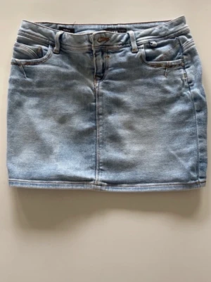 Ljusblå jeanskjol med fickor - Säljer en ljusblå jeanskjol i klassisk modell med fem fickor och bälteshällor. Kjolen har en kort passform och är tillverkad i denim med snygga söm-detaljer. Perfekt för dig som gillar en enkel och stilren look.