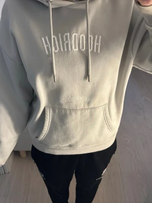 Grå Hoodrich hoodie - Snygg beige hoodie från Hoodrich med broderad logga på bröstet och 