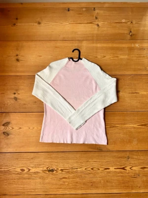 Ljusrosa stickad tröja från Tommy Hilfiger - Snygg ljusrosa tröja från Tommy Hilfiger med vita raglanärmar. Tröjan har en smal passform och ribbad halsringning. Tillverkad i Japan och perfekt för dig som gillar stilrena och klassiska plagg med en twist. 100% bomull