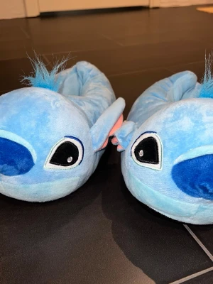 Stitch Tofflor Blå - Ett par tofflor med Stitch-motiv. Tofflorna är blå och har detaljer som öron och ansiktsdrag som liknar karaktären Stitch. ONESIZE