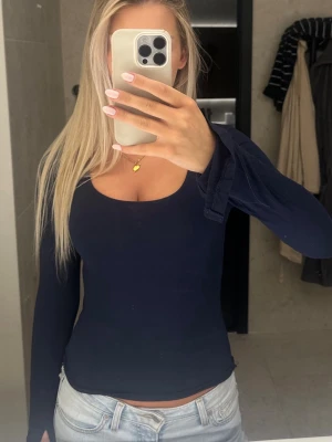 Mörkblå långärmad topp - mörkblå långärmad topp med rundad urringning och utsvängda ärmar med slits . Figurnära passform. 