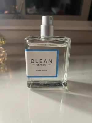CLEAN Classic Pure Soap parfym - Fräsch parfym från CLEAN Classic i doften Pure Soap. Flaskan är genomskinlig och fyrkantig med en enkel vit etikett och blå kant. Spraymunstycke i silverfärg. Perfekt för dig som gillar rena och lätta dofter. 85% kvar