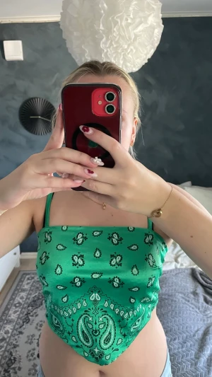 Grön bandana crop top med mönster - Trendig grön bandana crop top med vita paisleymönster och tunna axelband. Toppen knyts i ryggen. Perfekt till sommaren och festivaler. Materialet ser ut att vara mjukt och lätt, troligen polyester.