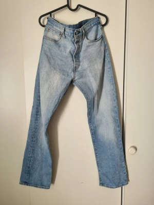 Levi's Premium ljusblå raka jeans - Ljusblå raka jeans från Levi's Premium med klassisk femficksdesign och hög midja. Jeansen är tillverkade i 100% bomull och har en snygg vintagekänsla med subtila slitningar. Perfekta för en avslappnad och trendig look. Sparsamt använda i fint skick. 