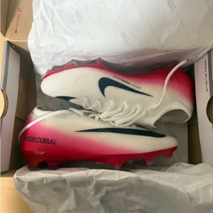 Nike Mercurial - Snygga Nike Mercurial fotbollsskor i vitt med röda och svarta detaljer. Skorna har en aerodynamisk form, stora svarta swoosh-loggor och röd sula med dobbar för bra grepp på planen. Ovandelen är i lätt syntetmaterial för optimal bollkontroll. Användes kort då jag åkte på långtidsskada. Kom gärna med bud så kan vi lösa något, skickas samma dag!