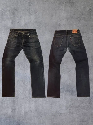 Feta Levi's 514  - Säljer ett par Levi's 514 jeans i svart tvätt med klassisk femficksdesign och raka ben. Jeansen har snygga slitningar och kontrastsömmar. Tillverkade i bomull med en cool vintagekänsla. Perfekta för dig som gillar tidlös streetstil.