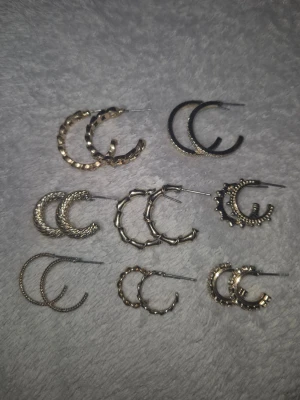 Set med 8 par örhängen i guld och svart - Säljer ett set med 8 par örhängen i olika former och mönster i guldfärg. Designen varierar mellan släta, räfflade och med nitar. Perfekta hoops för att mixa och matcha till olika stilar. Har gjorts rent med alkohol såklart! Kommer även med ploppar till varje par.