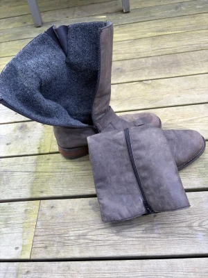 Grå fodrade läderstövlar med spännen Rieker - Säljer ett par gråa stövlar i läder med två snygga metallspännen på skaftet och dragkedja på insidan. Insidan är fodrad med mjukt grått tyg som håller värmen. Sulan är i brunt träutseende och stövlarna har en cool, robust look.