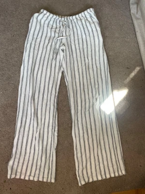 Randiga vita linnebyxor - Säljer ett par vita linnebyxor med svarta vertikala ränder och avslappnad passform. Byxorna har resår i midjan och dragsko för extra komfort. Perfekta för en chill och stilren look under varma dagar.super fina hör av dig för frågor💓💓