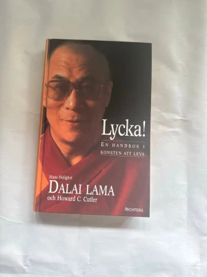 Lycka! Dalai Lama & Howard C. Cutler - En bok med titeln 'Lycka! En handbok i konsten att leva' av Dalai Lama och Howard C. Cutler. Omslaget är i röd, svart och orange ton med vit text. Boken är inbunden och har ett porträtt på framsidan. Perfekt för dig som vill läsa om livsfilosofi och personlig utveckling.