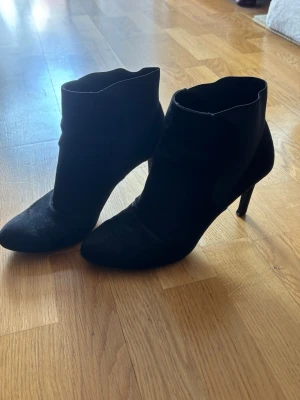 Svarta höga stövletter i mocka - Snygga svarta stövletter med spetsig tå och smal klack. Tillverkade i mocka med en stilren och enkel design. Perfekta för dig som vill ha en klassisk och trendig look.