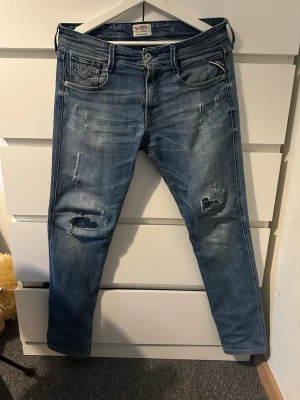 Blå slitna jeans från replay - Säljer ett par blå jeans från replay jeansen har klassisk femficksdesign, dragkedja och knapp i midjan. Materialet är bomull med en skön stretch. Perfekta för en avslappnad och trendig look.
