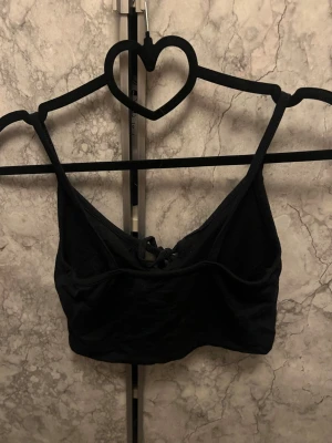 Svart magtröja med snörning fram - En svart bralette med smala axelband och snörningsdetalj framtill. Mjuk och bekväm modell utan bygel, perfekt för en avslappnad stil. Materialet ser ut att vara bomull eller bomullsblandning.
