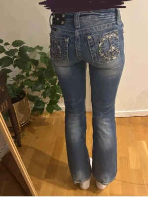 Miss me jeans - Säljer ett par blå miss me bootcut jeans med slitningar och peace-märken i paljetter på bakfickorna. Jeansen har låg midja, femficksmodell och detaljer vid fickorna. Midjemått: 33cm.🩷 Innerbenslängd: 74cm.🩷