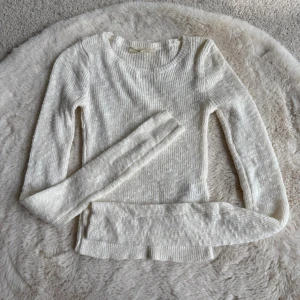 Vit stickad tröja från Hollister - Snygg vit stickad tröja från Hollister med rund halsringning och långa ärmar. Tröjan har en smal passform och är ribbstickad, vilket ger en stilren och enkel look. Perfekt att matcha med jeans eller kjol. OBS mindre i strl, skulle säga S 