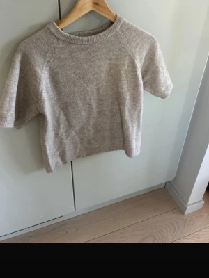 Beige stickad kortärmad tröja 157 - Stickad tröja i mjuk beige nyans från 157 med korta ärmar och ribbad halsringning. Perfekt för lager-på-lager och enkel att matcha med jeans eller kjol. Materialet är ullblandning och ger en skön känsla. Enkel och stilren design.