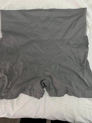 Grå träning shorts med hög midja - Säljer ett par grå tränings shorts med hög midja som formar och slätar ut siluetten. Sömlös design för extra komfort och diskret look under kläder. Materialet är stretchigt och andas, perfekt för att ge stöd och en smickrande passform.