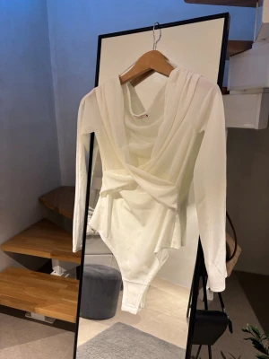 Vit långärmad body från Nelly - Snygg vit body från Nelly med långa ärmar och djup omlott-ringning framtill. Tillverkad i ett mjukt och stretchigt material som sitter skönt på kroppen. 