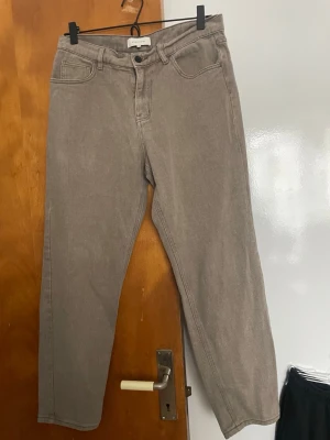 Beige raka jeans från Studio Total - Snygga beige jeans från Studio Total med rak passform och klassisk femficksdesign. Jeansen har hög midja, bälteshällor och stängs med knapp och dragkedja. Perfekta för en avslappnad och trendig look.