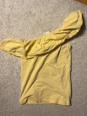Gul off shoulder topp från Kappahl - Storlek 146/152 men skulle säga att den passar xs och kanske xxs. Endast använd ca 3 ggr. Jättefin på sommaren!Snygg gul off shoulder topp från Kappahl med volang runt axeln. Tunn och mjuk bomullskvalitet, perfekt för varma dagar. Trendig och bekväm modell som ger en cool vibe till din outfit. 