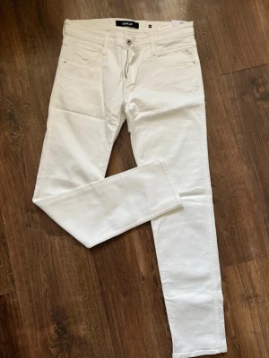 Replay jeans vita - Snygga vita jeans från Replay i modellen Anbass. De har en slim fit passform, klassisk femficksdesign och dragkedjegylf. Materialet är mjukt och stretchigt för extra komfort. Perfekta för dig som vill ha en clean och fräsch look. Inga defekter helt nya har dock tagit av lappen men samma skick!