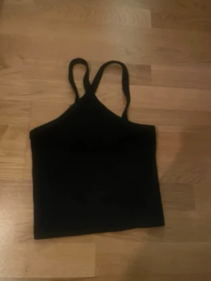 Svart ribbad linnetopp - Svart ribbad linnetopp med smala axelband och croppad passform. Perfekt för att styla med jeans eller kjol. Enkel och stilren design som passar till många olika looks.