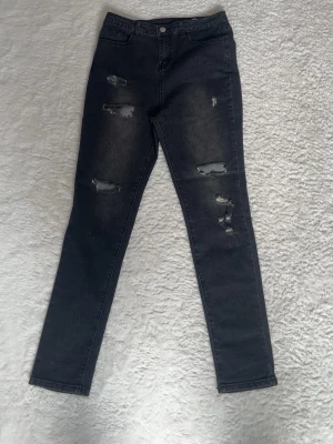 Svarta skinny jeans med slitningar - Snygga svarta skinny jeans med flera slitningar på benen och lätt tvättad look. Jeansen har klassisk femficksmodell och hög midja. Perfekta för en trendig och avslappnad stil.