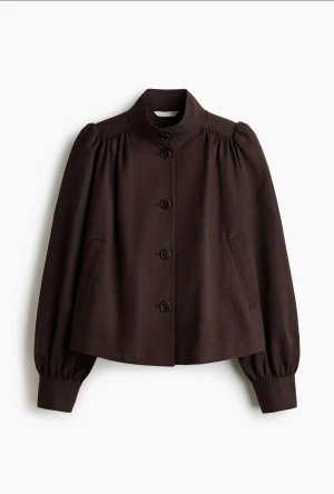 Brun kort jacka med puffärm - Snygg brun jacka med hög krage och puffiga långärmar. Jackan är croppad och har knappar framtill samt fickor på sidorna. Perfekt för dig som vill ha en stilren men trendig look.