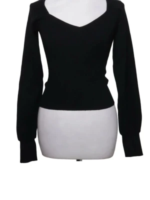 Svart stickad tröja med v-ringning - Snygg svart stickad tröja med djup v-ringning och långa ärmar. Tröjan har en figurnära passform och ribbstickade muddar vid ärmslut och nederkant. Perfekt att matcha med jeans eller kjol för en trendig look.