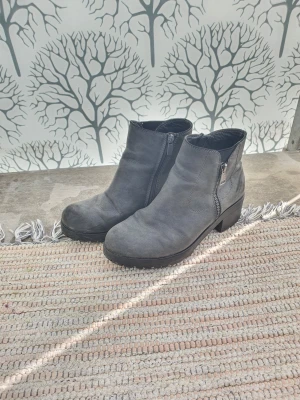 Gråa stövletter med dragkedja - Snygga gråa stövletter med grov sula och låg klack. Skorna har dragkedja på sidan för enkel på- och avtagning och är tillverkade i ett matt, mockaliknande material. Perfekta till jeans eller kjol för en cool look.