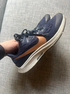 Nike blå sneakers med kopparfärgat Nikemärke - Snygga sneakers från Nike i mörkblått med kopparfärgat Nikemärke på sidan. Ovandelen är i meshmaterial för bra andningsförmåga. Storlek 38