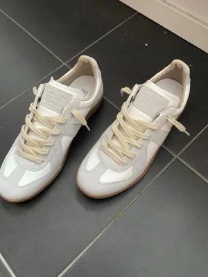 Vita sneakers med beige detaljer - Snygga vita sneakers med beige mockadetaljer och krämfärgade skosnören. Skorna har en klassisk låg siluett och gummisula i brunt. Perfekta för en clean och stilren look. Materialmix av läder och mocka.