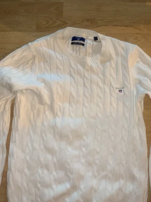Vit lstickad tröja från Gant - Säljer en klassisk vit kabelstickad tröja från Gant i premium bomull. Tröjan har rund halsringning, ribbade muddar och Gant-logga broderad på bröstet. Perfekt för dig som gillar stilrena och tidlösa plagg. Köpt för ca 1200kr. Knappt använd ca 1-3 gånger. 