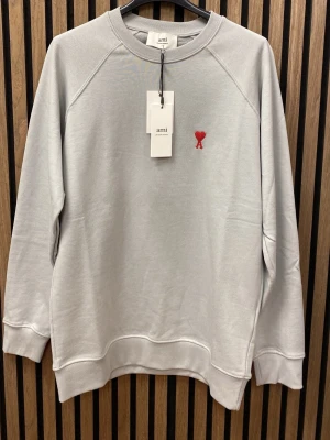 Grå sweatshirt  - Snygg grå sweatshirt med klassisk rund halsringning och röd broderad logga med hjärta på bröstet. Tröjan har ribbade muddar vid ärmslut och nederkant. Perfekt för en clean och stilren look.