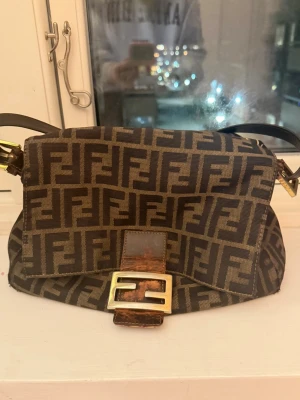 Fendi väska - Säljer min äkta Fendi väska i modellen mamma baguette💗  Väskan är inköpt för 2024 på vestiaire collective, finns bild och kvitto på mitt köp därifrån, så skickar gärna det om det skulle viljas🫶🏼   Väskan är i gott skick, men har några skavanker (se bilder) 🥰  Bredd: 28 cm Höjd: 22 cm Djup: 11,5 cm  Pris kan diskuteras!
