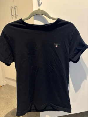 Svart t-shirt från GANT - Klassisk svart t-shirt från GANT med liten broderad logga på bröstet. Modellen är regular fit och har korta ärmar och rund halsringning. Tillverkad i mjuk bomull som känns skön mot huden. Perfekt basplagg till garderoben.