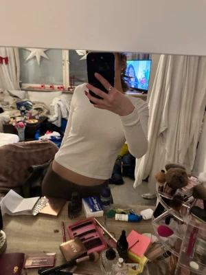 Vit långärmad croppad topp - Säljer en enkel och stilren vit långärmad topp med croppad passform. Perfekt att matcha med höga jeans eller kjol. Mjuk och skön, troligtvis i bomull eller polyester. Inga synliga detaljer eller mönster.