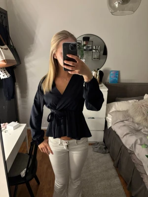 blå omlottblus med knytband - Snygg blå omlottblus med långa ärmar och knytband i midjan. Blusen har en djup v-ringning och lätt utsvängd nederkant. Perfekt att styla med jeans eller kjol för en trendig look.