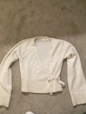 Vit omlottkofta med knytband - Snygg krämvit omlottkofta med knytband i midjan. Koftan har lång ärm och en mjuk, lite stretchig känsla. 💕💕