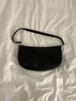 Svart axelremsväska i crocopräglat skinn - Snygg svart handväska med axelrem och crocopräglat mönster. Nästan oanvänd och väldigt rymlig 