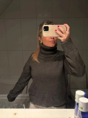 Mörkgrå stickad tröja med hög krage  - Mysig mörkgrå stickad tröja med hög krage, perfekt för vintern.